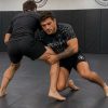 Two athletes grappling on BJJ mats, one wearing Reedot Sports spider web rash guard and shorts mid-roll